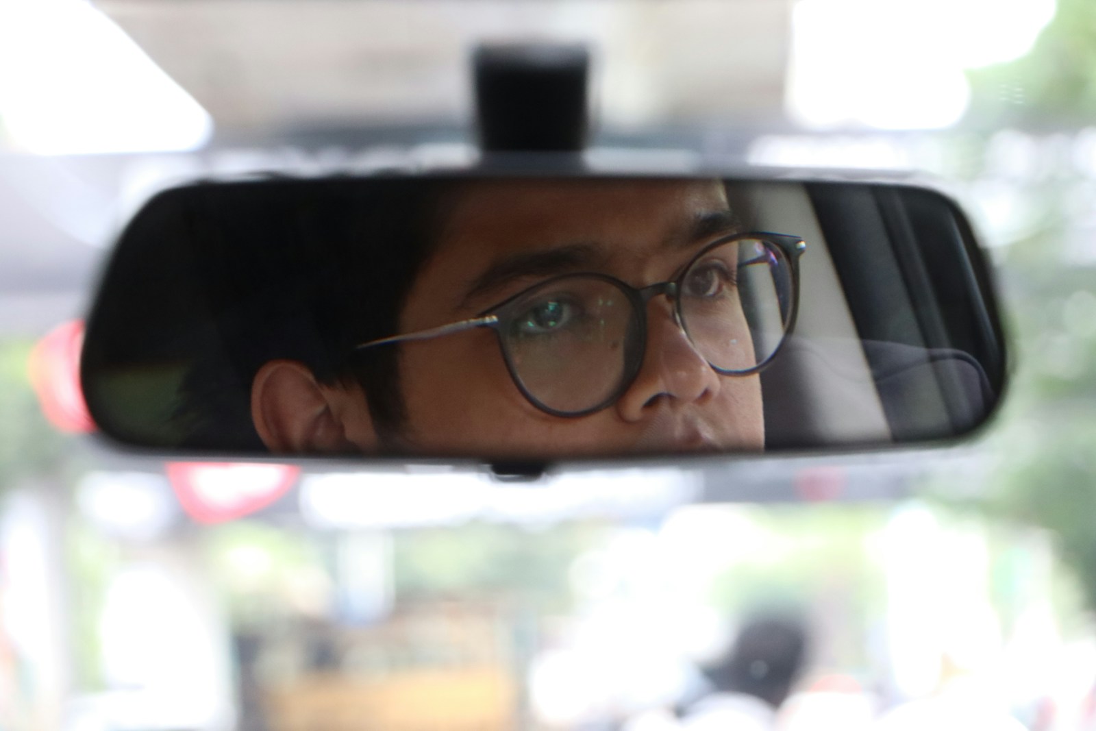 A man with glasses is seen in a rear view mirror